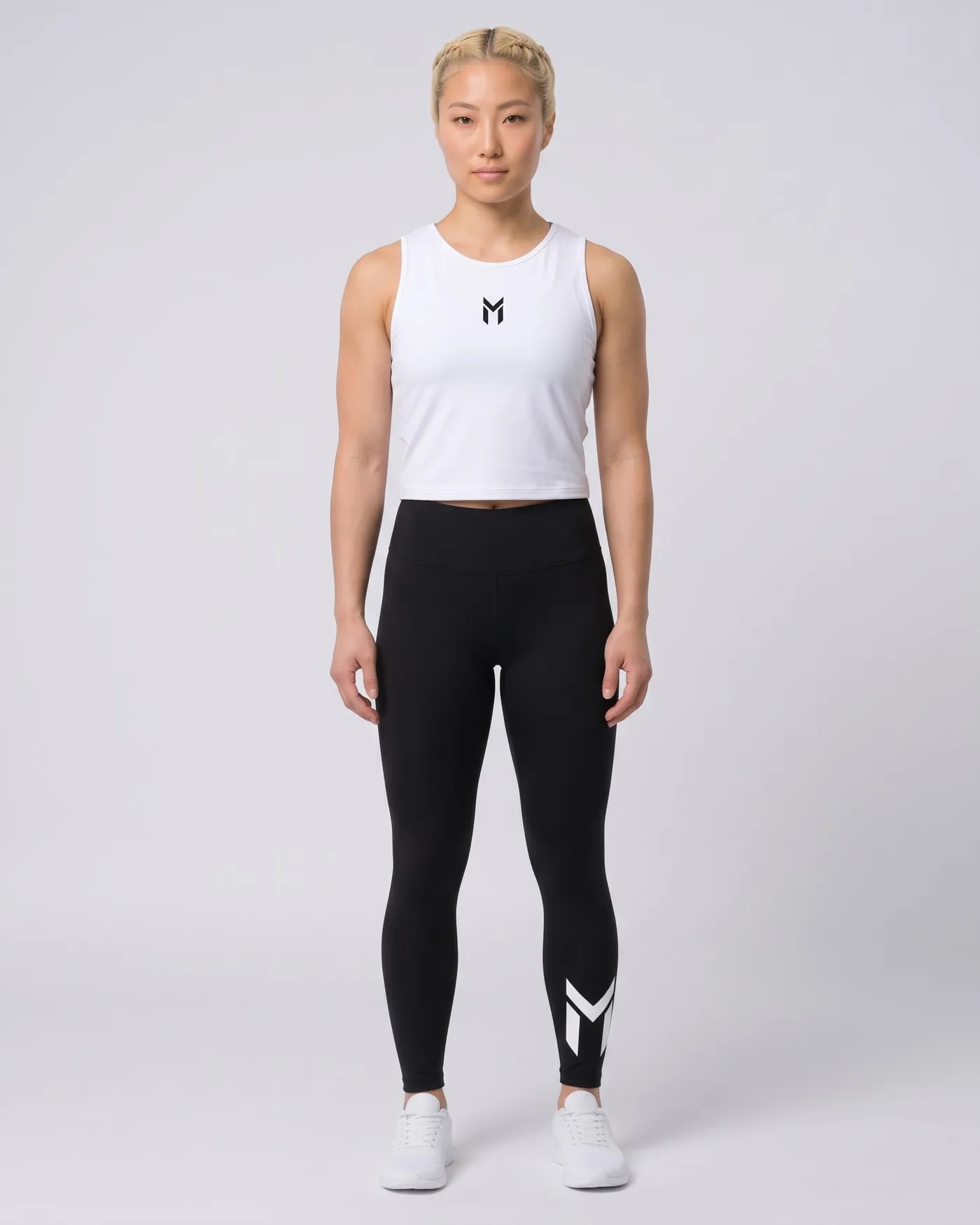 Person in weissem Crop Top und schwarzen Leggings vor hellgrauem Grund