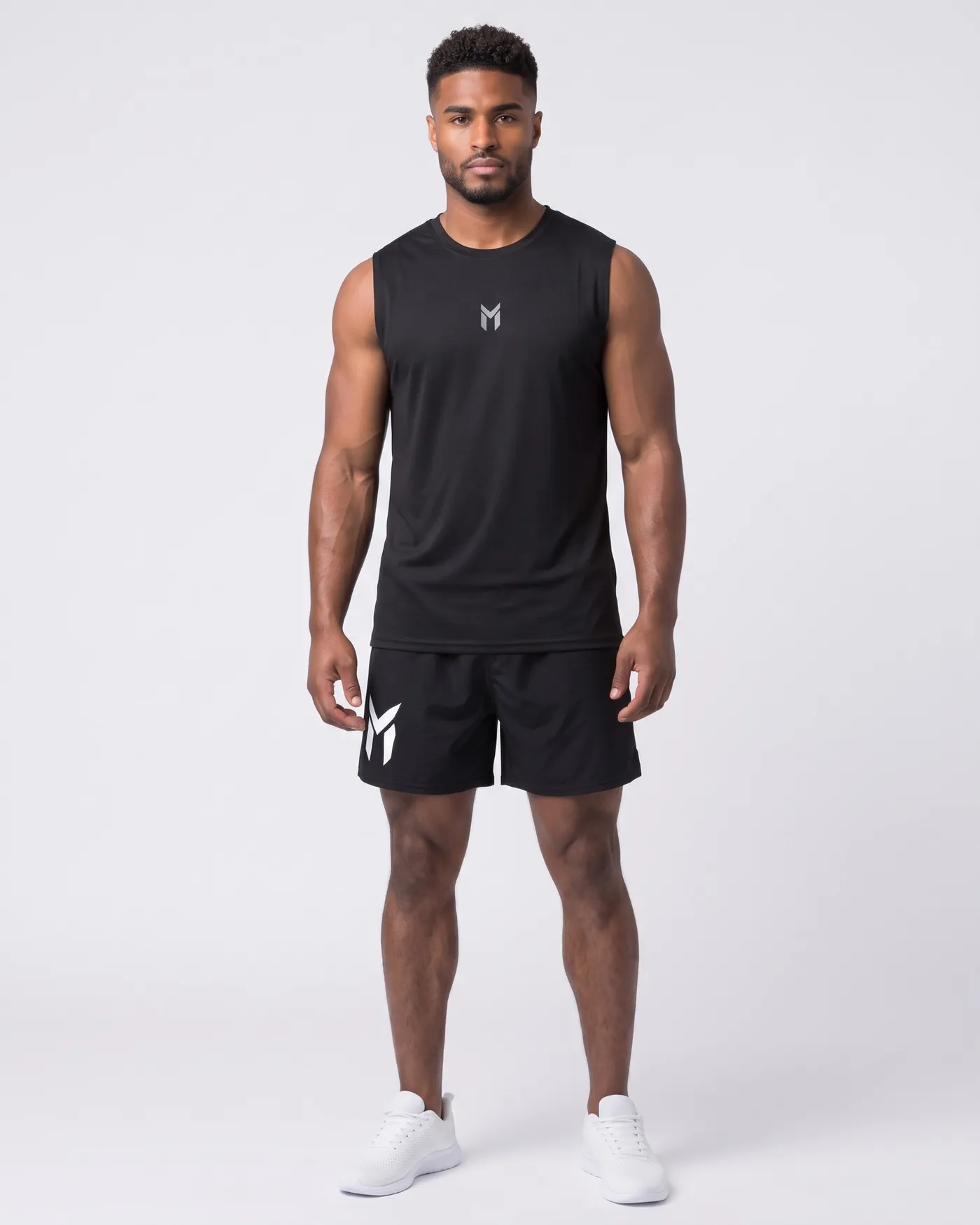 Person in schwarzem Tank und schwarzen Gym Shorts vor hellgrauem Grund