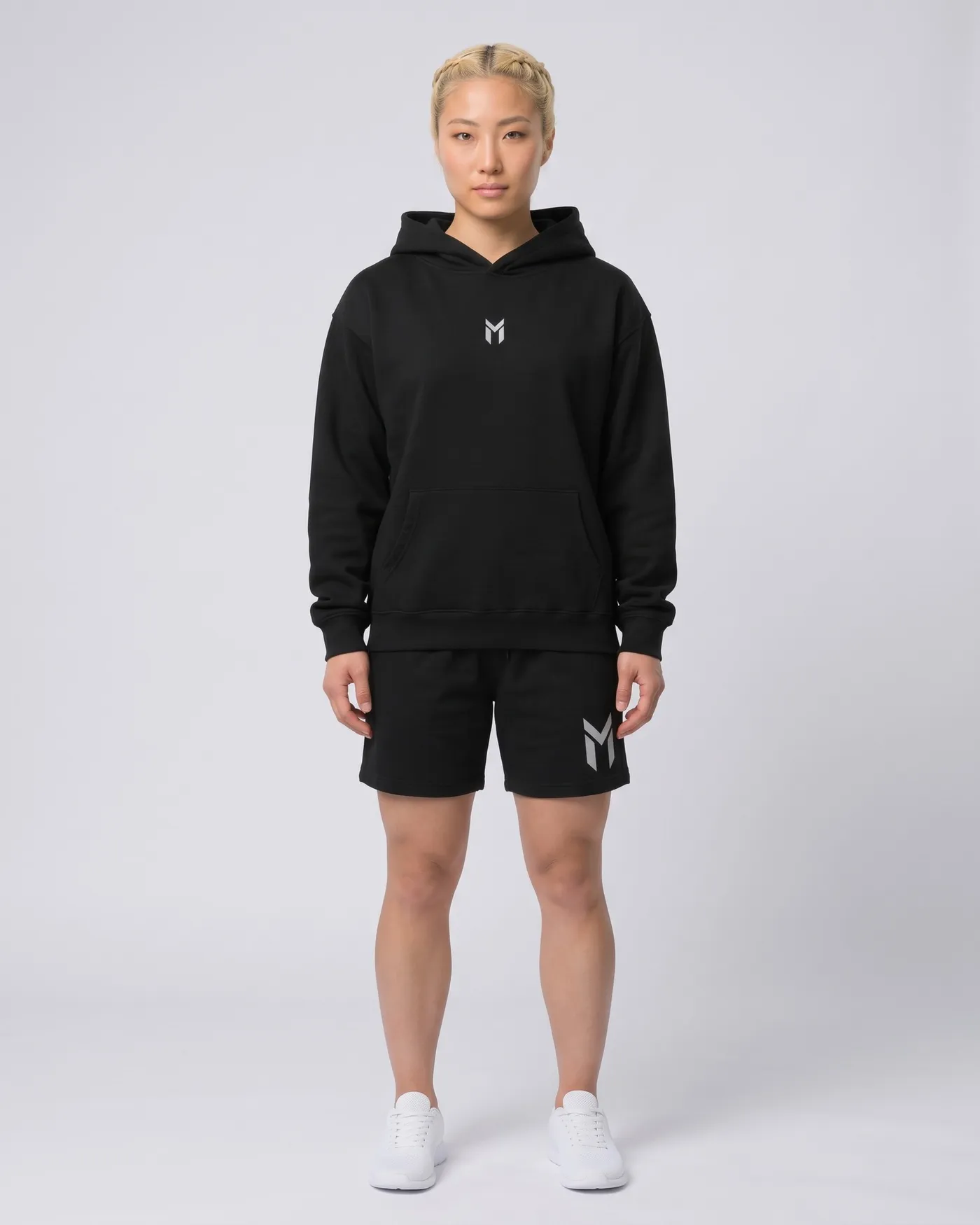 Person in schwarzem Oversized Hoodie und schwarzen Fleece Shorts vor hellgrauem Grund