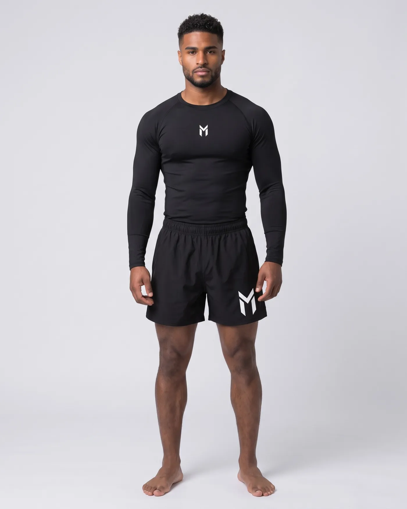 Person in schwarzem Compression Long Sleeve und schwarzen Muay Thai Shorts vor hellgrauem Grund